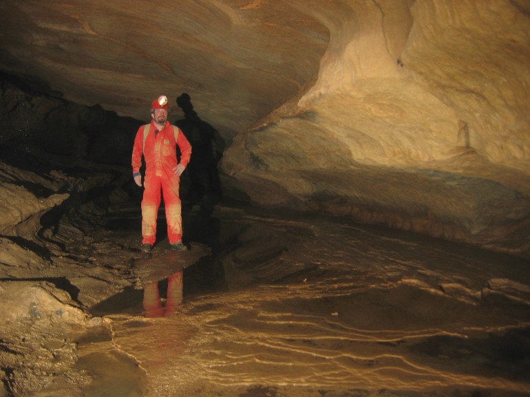 Rob standing in a fairly large passage, with a bit of water and some rimstone dams.